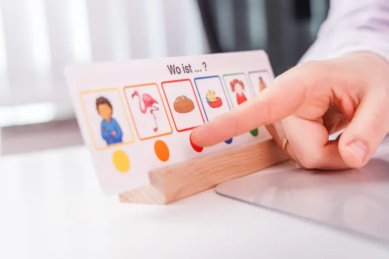 Hand zeigt auf eine Tafel mit Bildsymbolen zur unterstützten Kommunikation