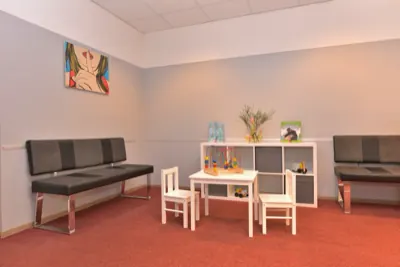 Wartebereich der Praxis mit Sitzbänken, kleinem Kindertisch und Spielregal